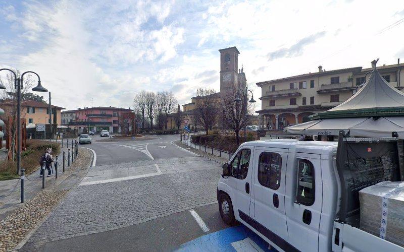 Un furgone bianco è parcheggiato su una strada asfaltata in una cittadina. Edifici, tra cui una torre dell'orologio, costeggiano lo sfondo. I pedoni camminano vicino ai marciapiedi acciottolati in una giornata parzialmente nuvolosa.