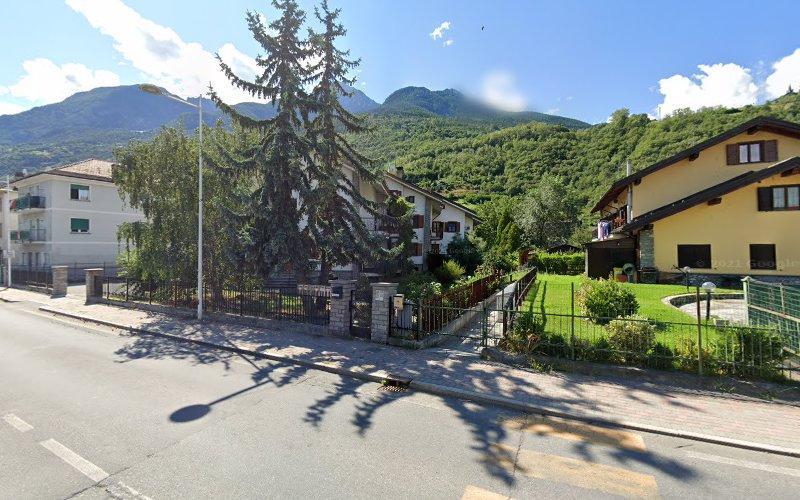 Una strada residenziale con case, alberi e una montagna sullo sfondo. La scena è soleggiata con un cielo azzurro terso.