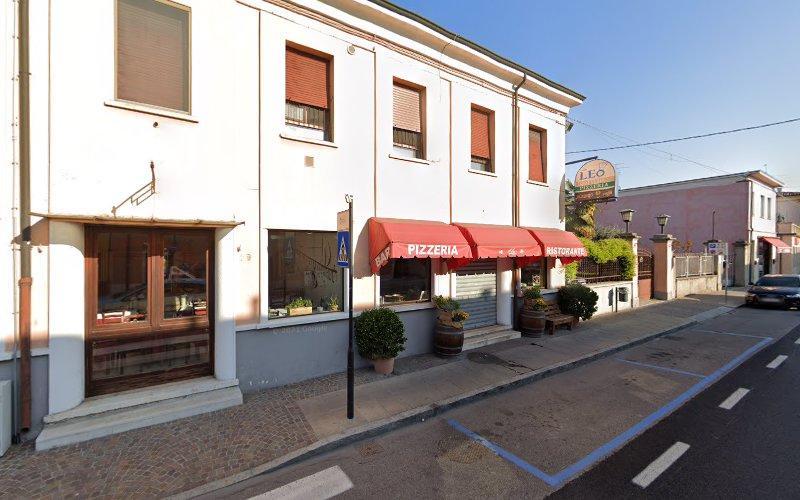 Vista stradale di un edificio a due piani che ospita una pizzeria e un ristorante con una tenda rossa, grandi finestre e due piante in vaso all'ingresso. Un'auto è parcheggiata lungo la strada.