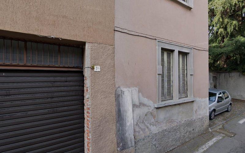 Un edificio beige con la vernice scrostata, una finestra con le persiane chiuse e la porta di un garage accanto a una piccola auto argentata parcheggiata sulla strada.