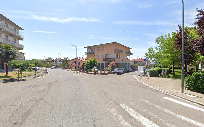 Un tranquillo incrocio di strade suburbane con edifici residenziali, auto parcheggiate, alberi e un cielo azzurro terso. Le strisce pedonali sono visibili sulla strada. Sono presenti segnali e lampioni.