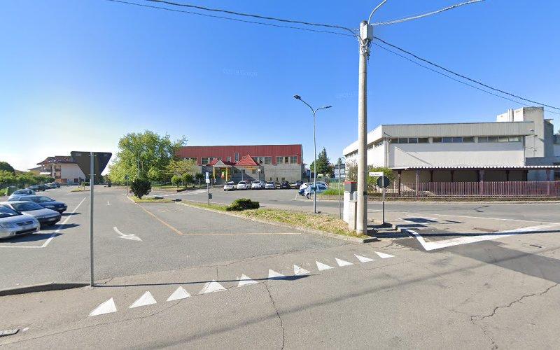 Un incrocio tranquillo con auto parcheggiate, segnali stradali ed edifici sullo sfondo, sotto un cielo azzurro e limpido.
