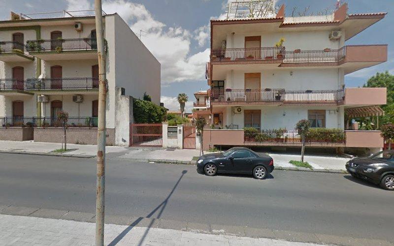 Due edifici residenziali a più piani con balconi si affacciano su una strada con auto parcheggiate. Il cielo è parzialmente nuvoloso.