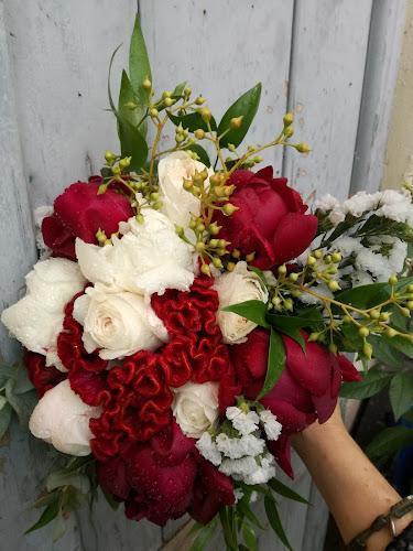 Una mano che regge un bouquet da sposa con rose rosse e bianche, verde e piccoli fiori bianchi, su uno sfondo di legno.