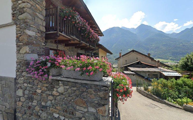 Un edificio in pietra con balconi decorati con fiori rosa, sullo sfondo le montagne in una giornata di sole.