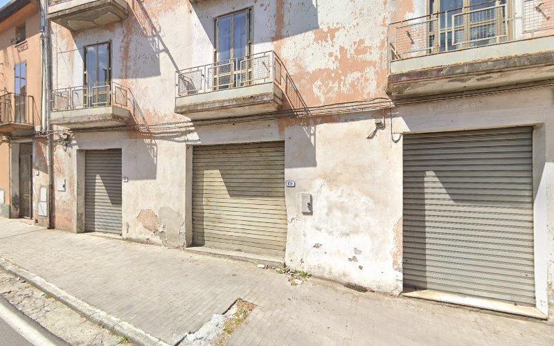 La facciata di un edificio usurato con tre porte avvolgibili metalliche chiuse e due balconi. Le pareti mostrano segni di vernice scrostata e usura. L'edificio si trova lungo uno stretto marciapiede.