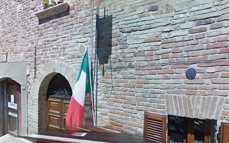 Edificio in mattoni con una porta di legno ad arco che espone una bandiera italiana. Nelle vicinanze, c'è una piccola finestra rettangolare con persiane di legno.