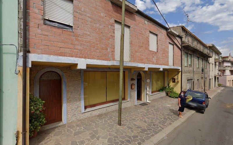 Vista stradale di un edificio con persiane chiuse e una porta di legno. Una persona è in piedi accanto a un'auto parcheggiata sul marciapiede asfaltato. Un palo è visibile di fronte all'edificio.