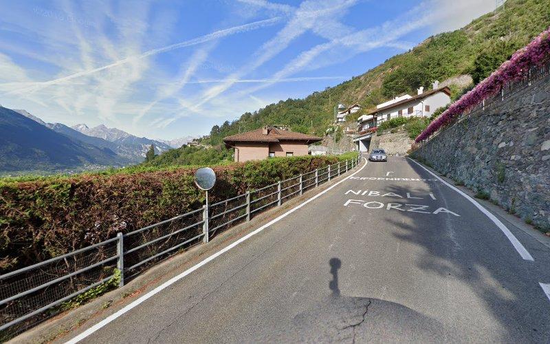 Una strada tortuosa in una zona montuosa con case sulla destra e colline verdi sulla sinistra. Le parole dipinte sulla strada recitano "Nibali Forza". Il cielo è limpido con scie di condensazione visibili.