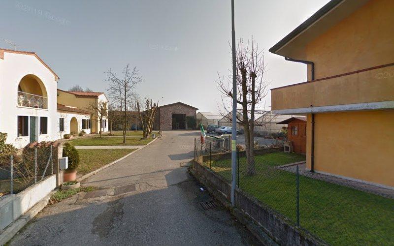 Veduta di una strada in una zona residenziale con un edificio giallo sulla destra, un edificio bianco sulla sinistra, alberi spogli, una strada stretta e una struttura alla fine della strada.