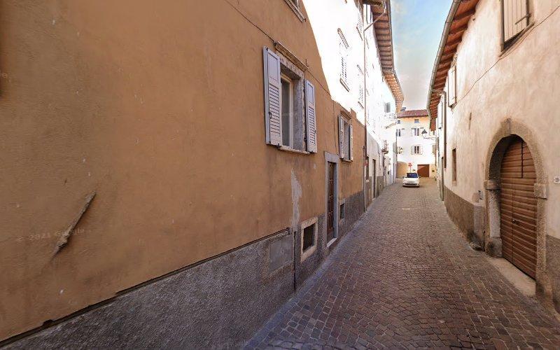Stretto vicolo acciottolato fiancheggiato da edifici intonacati beige e finestre con persiane. Un'unica macchina bianca è parcheggiata alla fine della strada.