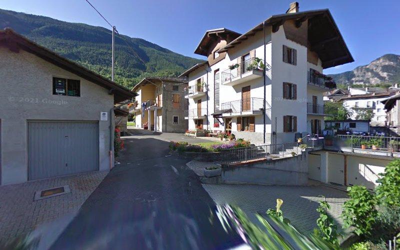 Un piccolo villaggio di montagna con case a più piani, balconi decorati con fiori, una strada stretta e tanto verde circostante.