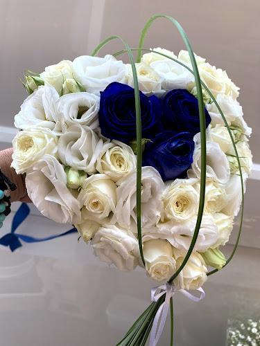 Una mano che regge un mazzo di rose bianche con tre rose blu al centro, avvolte da foglie verdi.