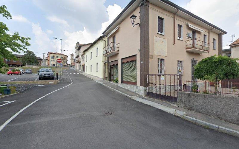 Una strada stretta in un quartiere residenziale con auto parcheggiate, edifici a due piani e un cielo nuvoloso. Un edificio ha un piccolo balcone e una vetrina.