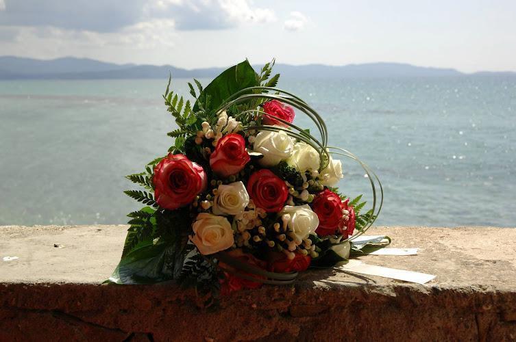 Un mazzo di rose rosse e bianche posto su una sporgenza con uno specchio d'acqua e montagne in lontananza sullo sfondo.