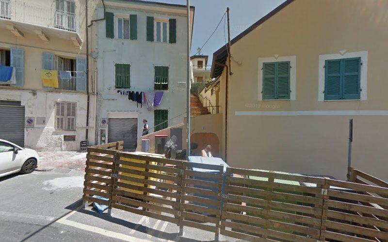 Una strada stretta delimitata da due edifici, con panni stesi ad asciugare su una corda e una staccionata di legno in primo piano. Una scala è visibile sullo sfondo.