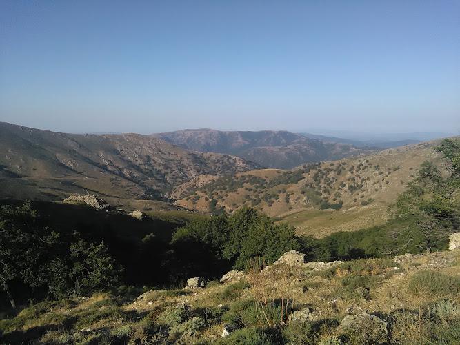 Un paesaggio montuoso sotto un cielo azzurro e terso, con dolci colline, vegetazione sparsa e cime in lontananza.