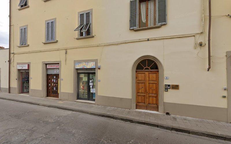 Un edificio color beige con diversi negozi, tra cui una libreria e un negozio d'arte, lungo una strada tranquilla. Sono visibili anche una porta di legno e persiane chiuse.