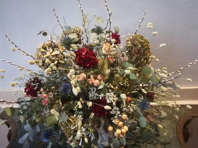 Una grande ed elaborata composizione floreale composta da un mix di fiori rossi, bianchi, blu e verdi, insieme a foglie e steli assortiti, esposta all'interno.