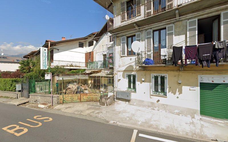 Vista stradale di un edificio residenziale con balconi, alcuni panni stesi, una porta da garage verde, un'area recintata con un piccolo giardino e una fermata dell'autobus segnalata sulla strada in primo piano.