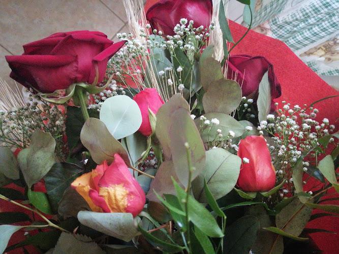 Un bouquet di rose rosse mescolate a verde e piccoli fiori bianchi, avvolto in carta rossa.