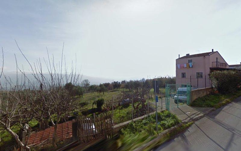 Una casa beige a due piani con i panni stesi sul balcone, situata lungo una strada in una zona rurale con alberi spogli e campi sullo sfondo sotto un cielo nebbioso.