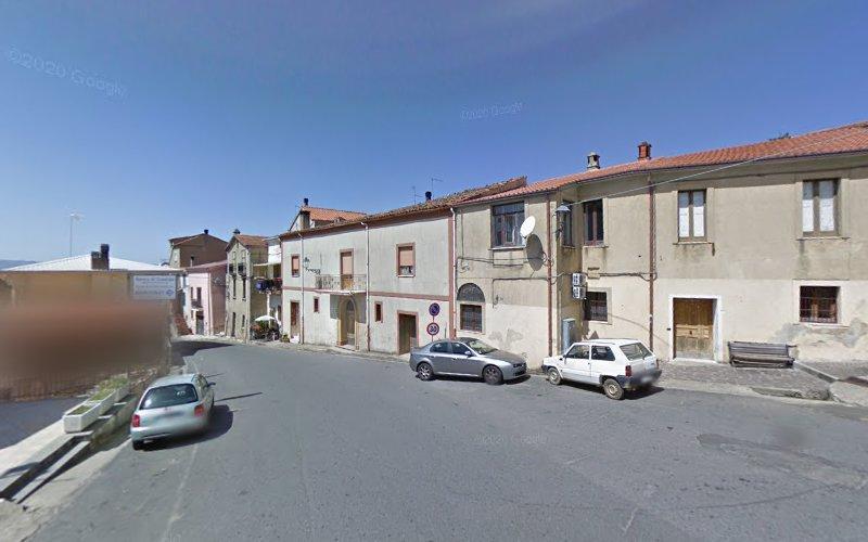 Una stradina tranquilla in un villaggio con qualche macchina parcheggiata, case modeste e un cielo azzurro e limpido.