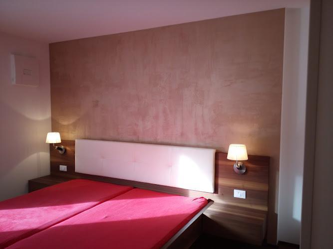 Una camera da letto con due letti singoli uniti, una testiera imbottita bianca, due lampade da comodino e una parete decorativa marrone chiaro.