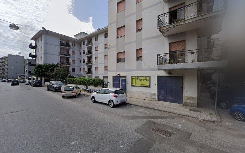Vista stradale di una zona residenziale con edifici residenziali a più piani. Diverse auto parcheggiate sono lungo il ciglio della strada e un piccolo negozio giallo è visibile al piano terra.