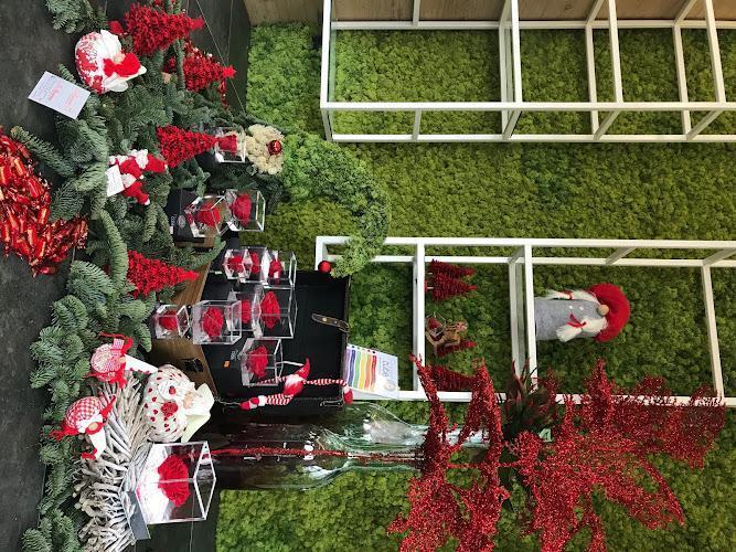 Esposizione di decorazioni natalizie rosse e bianche, tra cui piccoli alberi, gnomi e ornamenti, adagiate su un fogliame verde e su uno sfondo di muschio verde.