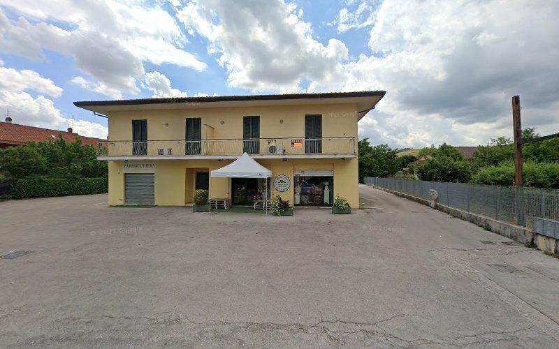Un edificio giallo a due piani con una piccola tenda da sole sopra un tavolo e delle sedie vicino all'ingresso. L'edificio è circondato da un'area pavimentata vuota e ha un cielo parzialmente nuvoloso sopra.