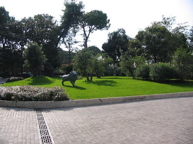 Un'area verde erbosa con una statua di leone, circondata da alberi, vicino a un sentiero lastricato in pietra.