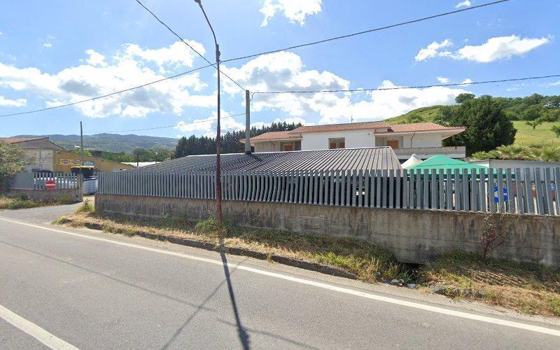 Vista stradale di un'area recintata con un edificio e una collina sullo sfondo in una giornata soleggiata con nuvole sparse.