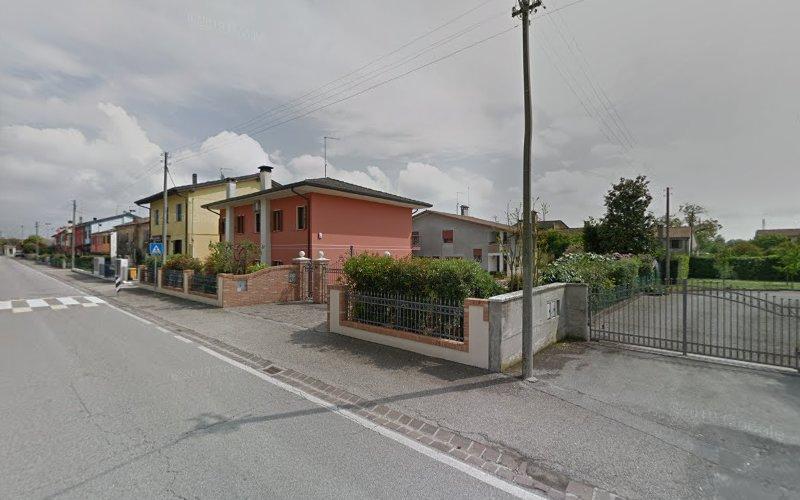 Una strada residenziale con case monofamiliari, tra cui una casa rossa con un vialetto d'accesso recintato e una casa gialla. Il marciapiede è delimitato da recinti e all'incrocio è visibile un attraversamento pedonale.