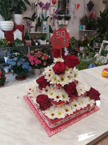 Una composizione floreale composta da rose rosse e margherite bianche disposte su più livelli, posizionata su un tavolo in una stanza piena di fiori e piante in vaso.