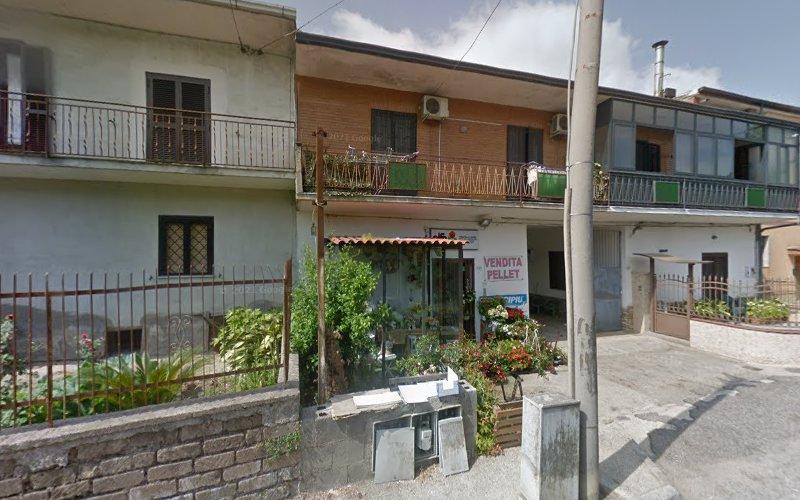 Fila di case collegate con balconi e piccoli giardini di fronte. Il cartello recita "Vendita Pellet". Alcune piante e una recinzione sono visibili in primo piano. Giornata di sole.