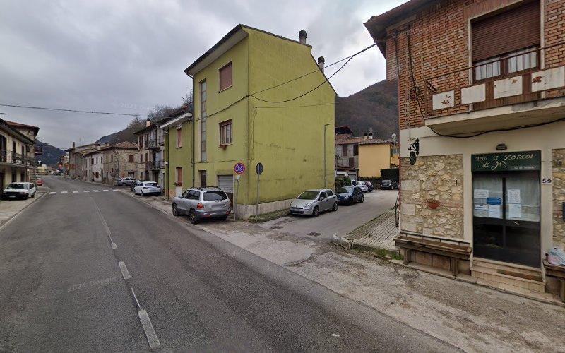 Una scena di strada con auto parcheggiate lungo un marciapiede. Gli edifici sono prevalentemente alti due o tre piani, uno verde e gli altri in mattoni. Il cielo è coperto. Ci sono colline sullo sfondo.