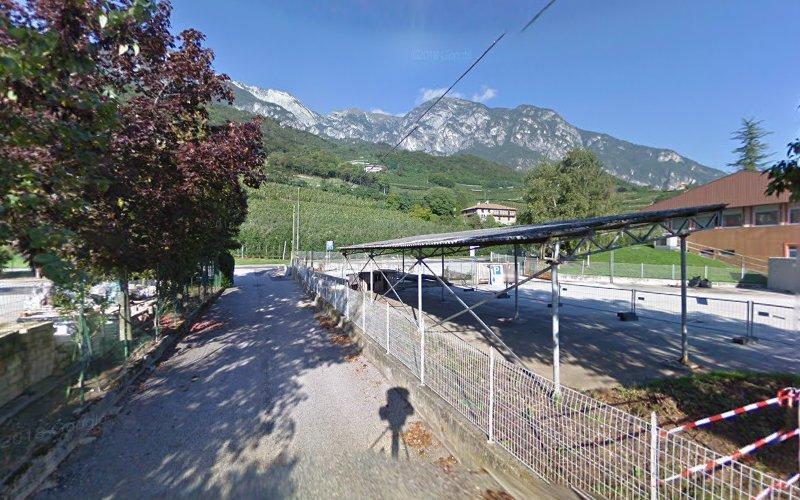 Un sentiero di ghiaia conduce a un'area recintata con strutture metalliche, immersa in uno scenario di montagne e verde sotto un cielo azzurro e terso.