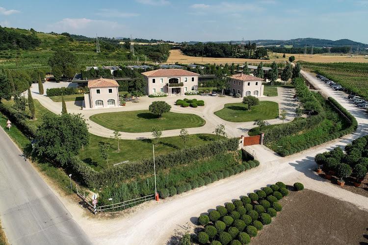 Vista aerea di una tenuta di campagna caratterizzata da due grandi edifici con tetti di tegole rosse, prati ben curati, vialetti circolari e campi e vegetazione circostanti.
