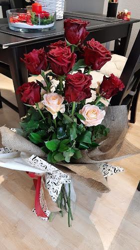 Un bouquet di rose rosse e rosa pallido disposte con fogliame verde e avvolte in tela di juta decorativa e tessuto fantasia, posizionato su un pavimento in legno accanto a un tavolo da pranzo.