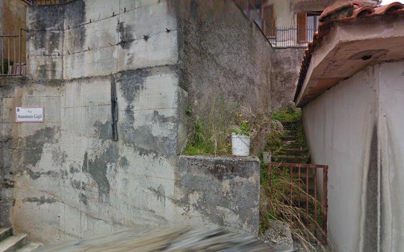 Struttura in cemento e scalinata ricoperta di vegetazione, con un secchio bianco posizionato lungo le scale. Un cartello sul muro recita "Ascanio Ciofi.