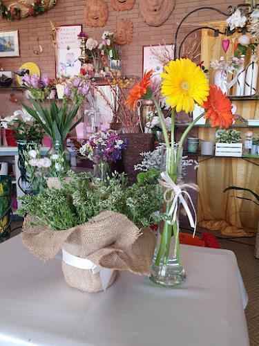 Esposizione di fiori in un negozio, con gerbere gialle e arancioni in un vaso di vetro e una varietà di piccoli fiori e verde avvolti in tela di juta su un tavolo.
