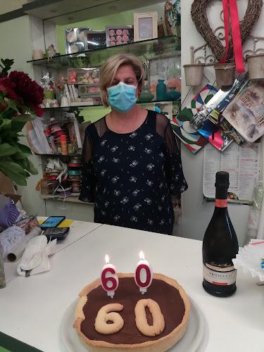 Una donna che indossa una mascherina è in piedi dietro un tavolo con una torta che ha il numero 60 come candeline. C'è una bottiglia di vino accanto alla torta.
