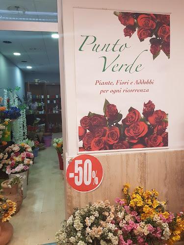 Un negozio di fiori con un grande cartello con la scritta "Punto Verde" e una varietà di fiori esposti. C'è un cartello rosso con la scritta "-50%" sul muro.