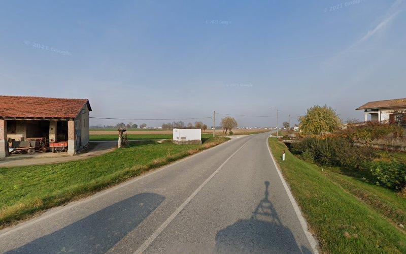 Una strada di campagna fiancheggiata da aree erbose e pochi edifici, con un cielo limpido e campi sullo sfondo.