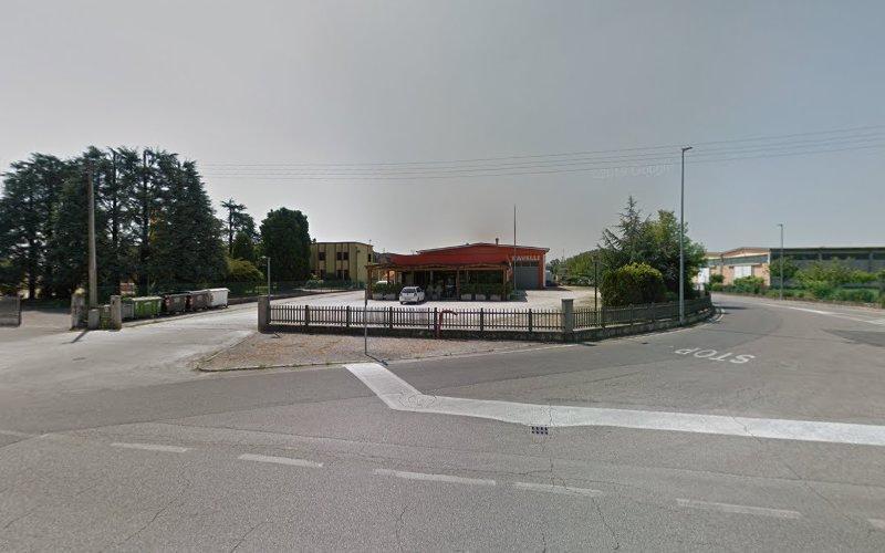 Una proprietà recintata con un grande edificio e alcuni alberi si trova a un incrocio stradale con segnali di stop su entrambi i lati. Un'auto bianca è parcheggiata di fronte all'edificio.