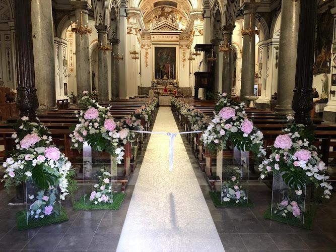 Interno della navata centrale di una chiesa decorata con un tappeto bianco e composizioni floreali con fiori rosa e bianchi, che conduce all'altare.