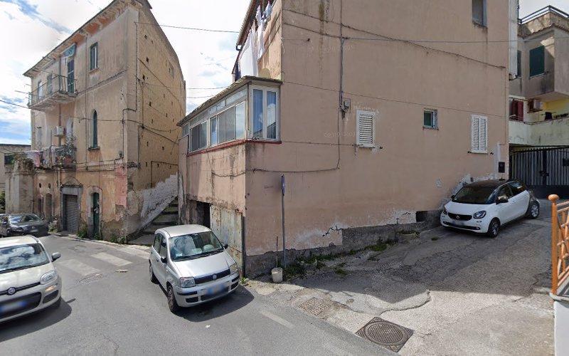 Un incrocio di strade strette con auto parcheggiate ed edifici con esterni rovinati dalle intemperie. Un edificio ha una scalinata che conduce a un ingresso. Un'altra auto è parcheggiata su una leggera pendenza.
