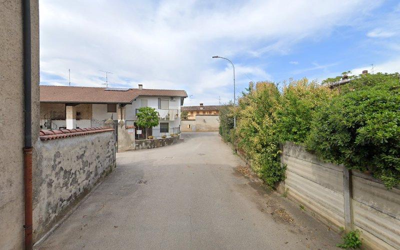 Una stretta strada residenziale fiancheggiata da case e vegetazione lussureggiante sotto un cielo nuvoloso. Si vede un lampione e la strada curva leggermente più avanti.
