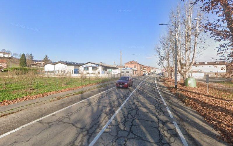 Un'auto rossa percorre una strada a due corsie fiancheggiata da case e alberi spogli in una giornata limpida. La strada mostra segni di usura e presenta alcune crepe.